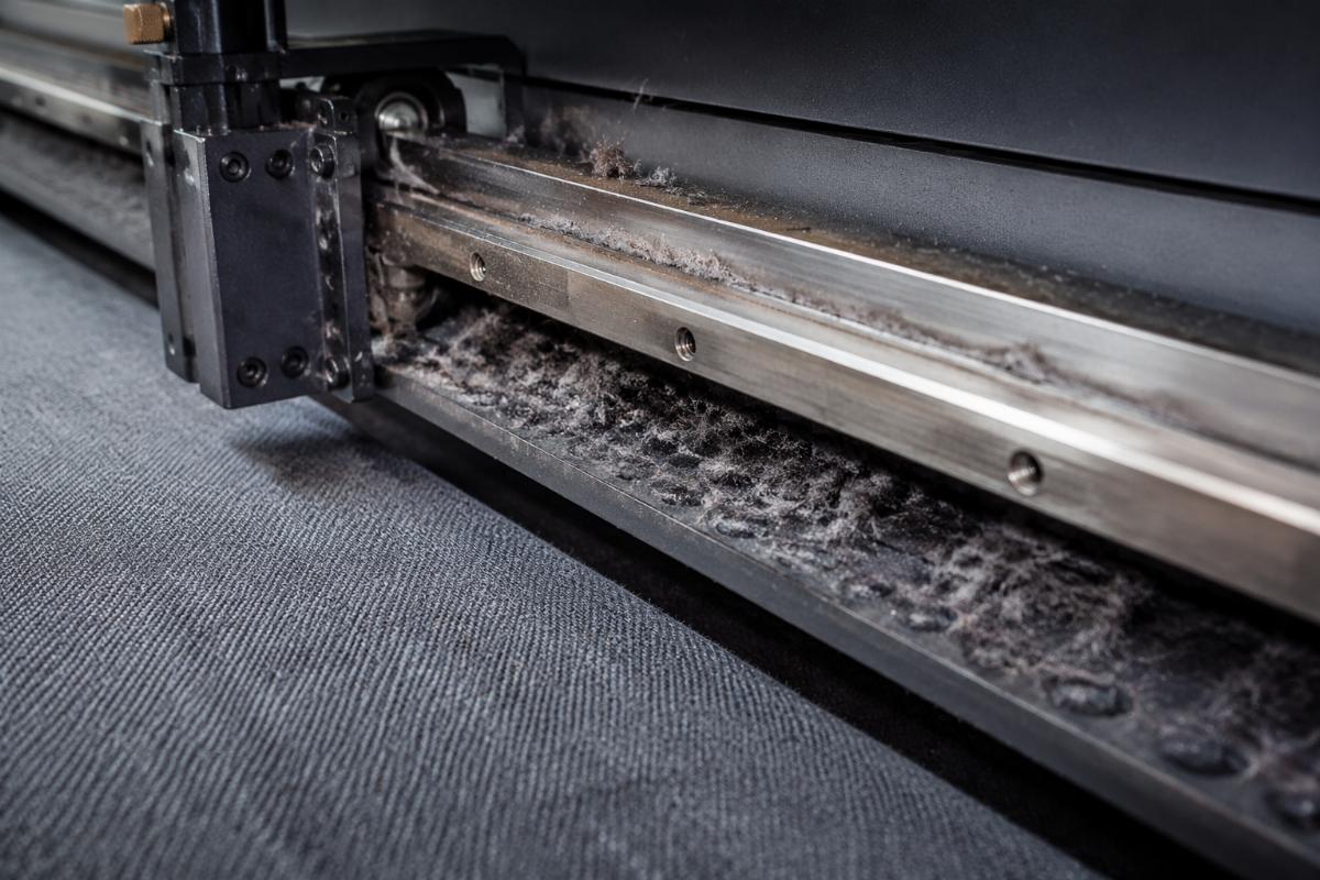 Close-up view of fabric cutting machine guide rail showing dust and lint accumulation